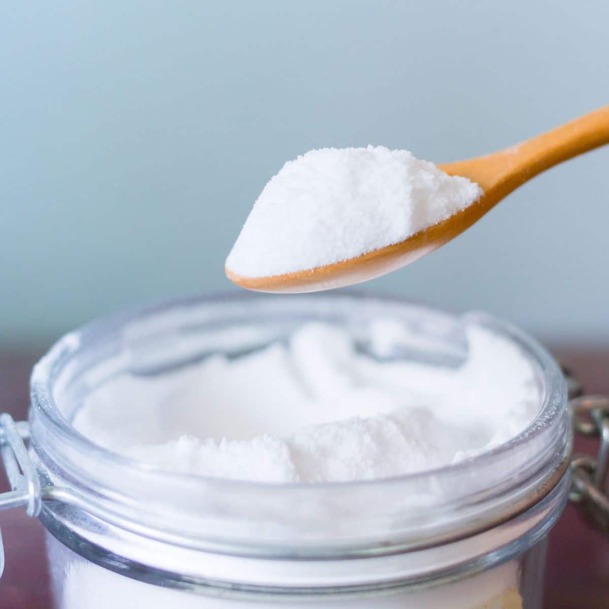 Wooden spoon holding homemade dishwasher detergent above glass jar filled with detergent.