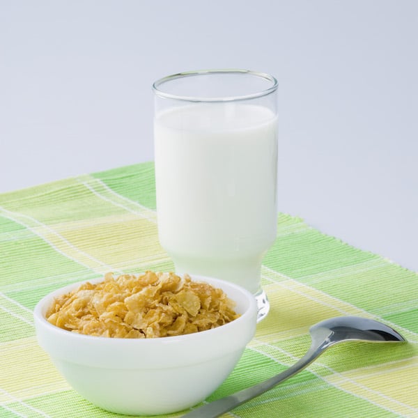 glass of milk with bowl of cereal and spoon