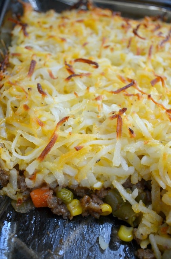 Hashbrown Hamburger Casserole with Frozen Vegetables and Cheese in Glass Dish with One piece missing