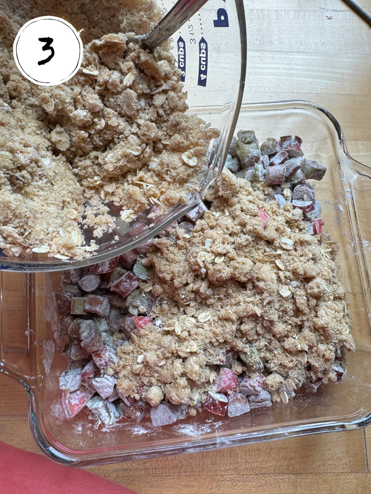 Pouring crumb topping mixture on top of rhubarb flour and sugar mixture.