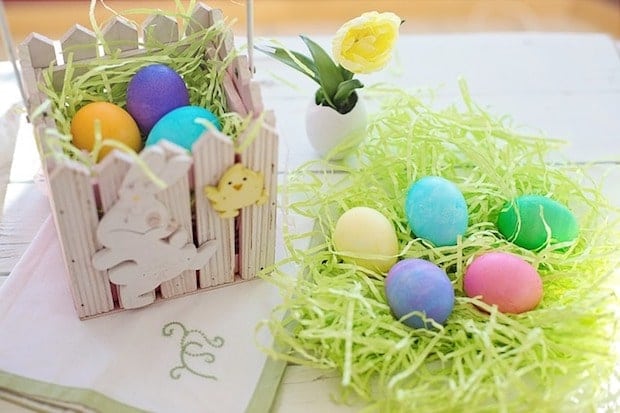 easter eggs in wooden box and on table in pile of easter grass