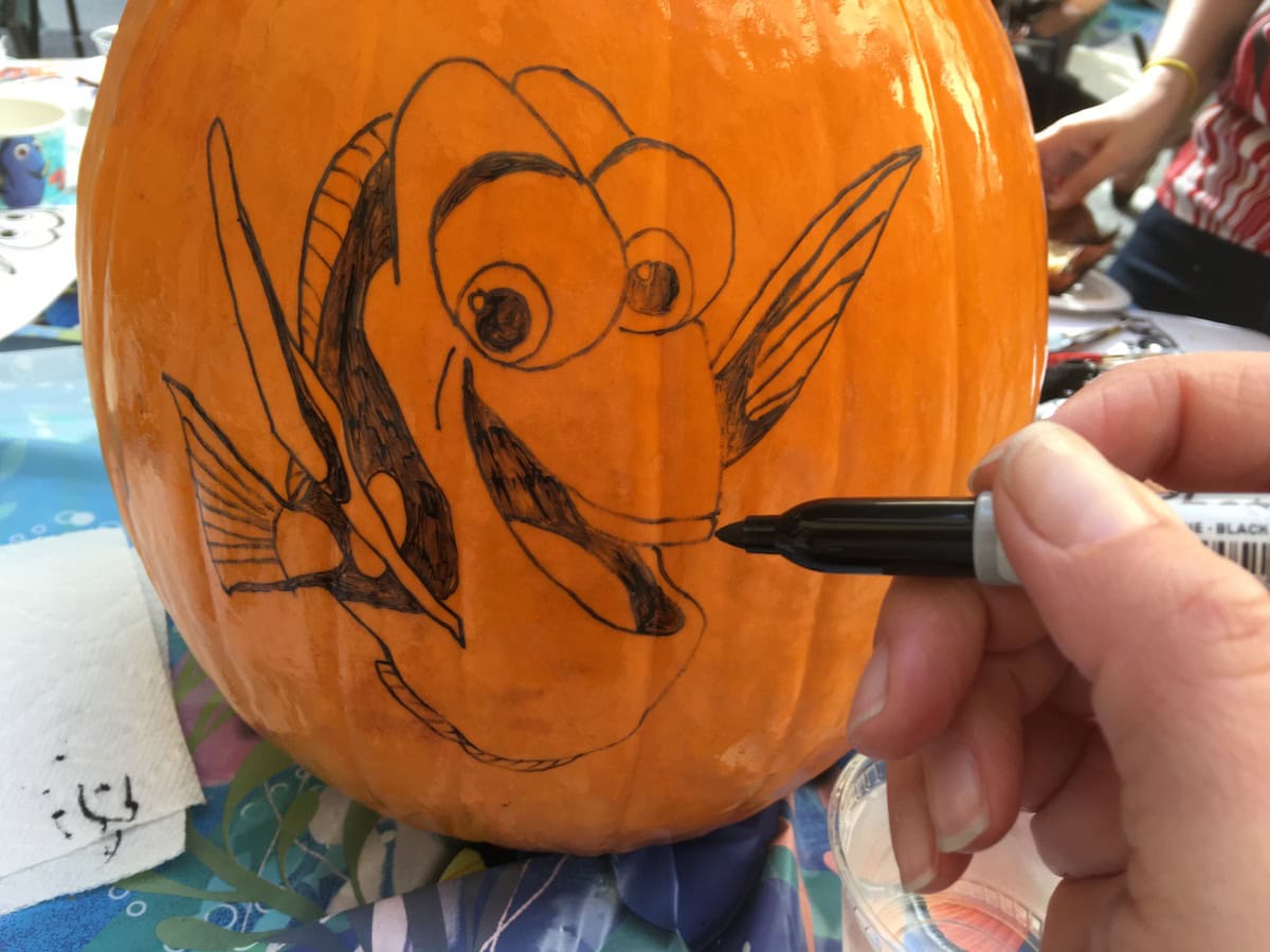 Using black Sharpie to outline Dory pumpkin stencil for a carved and painted Halloween decoration.