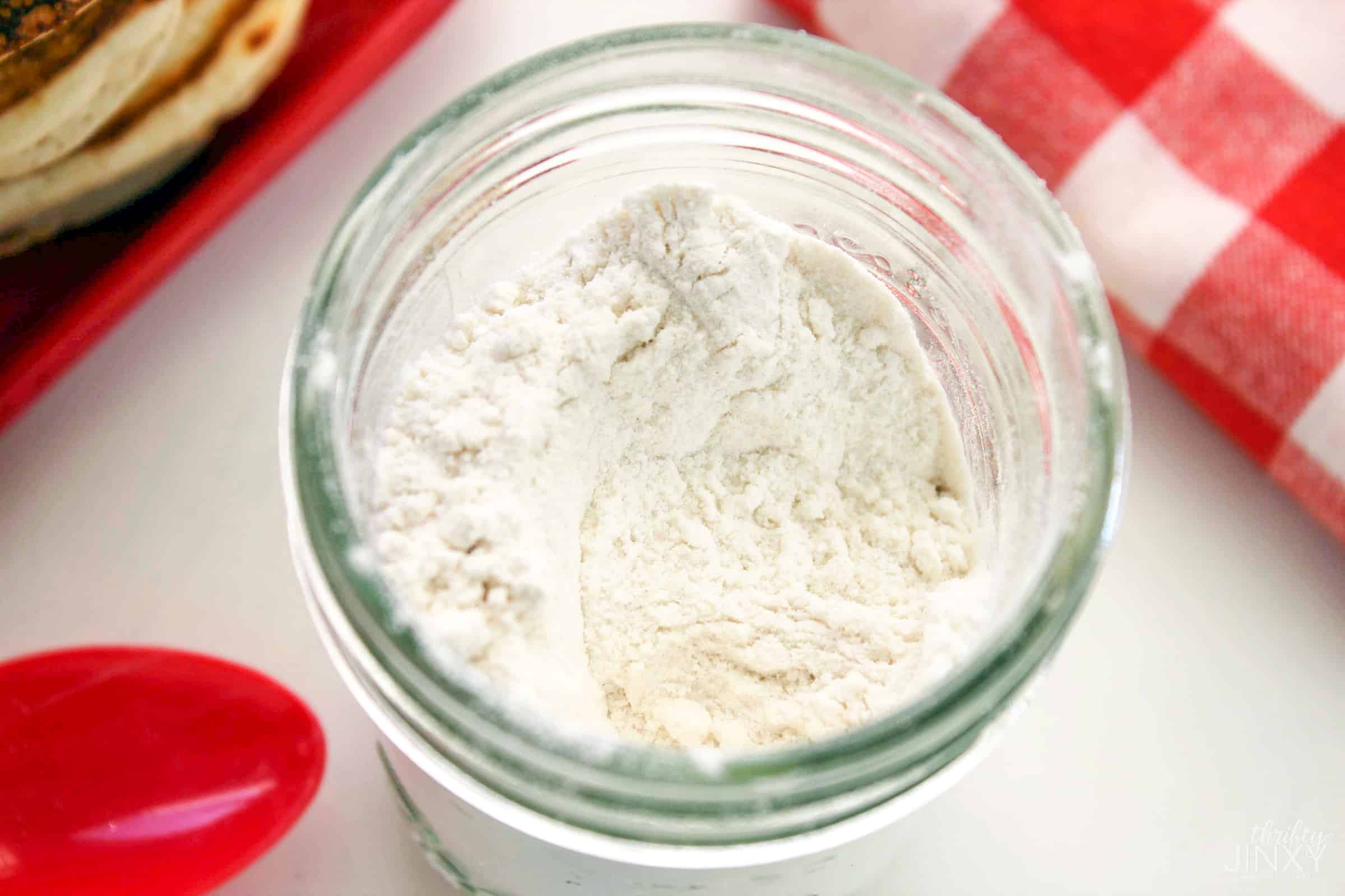 Glass jar with Homemade Pancake Mix next to a stack of pancakes and red checked towel.