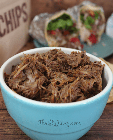 beef barbacoa in bowl with burritos in background