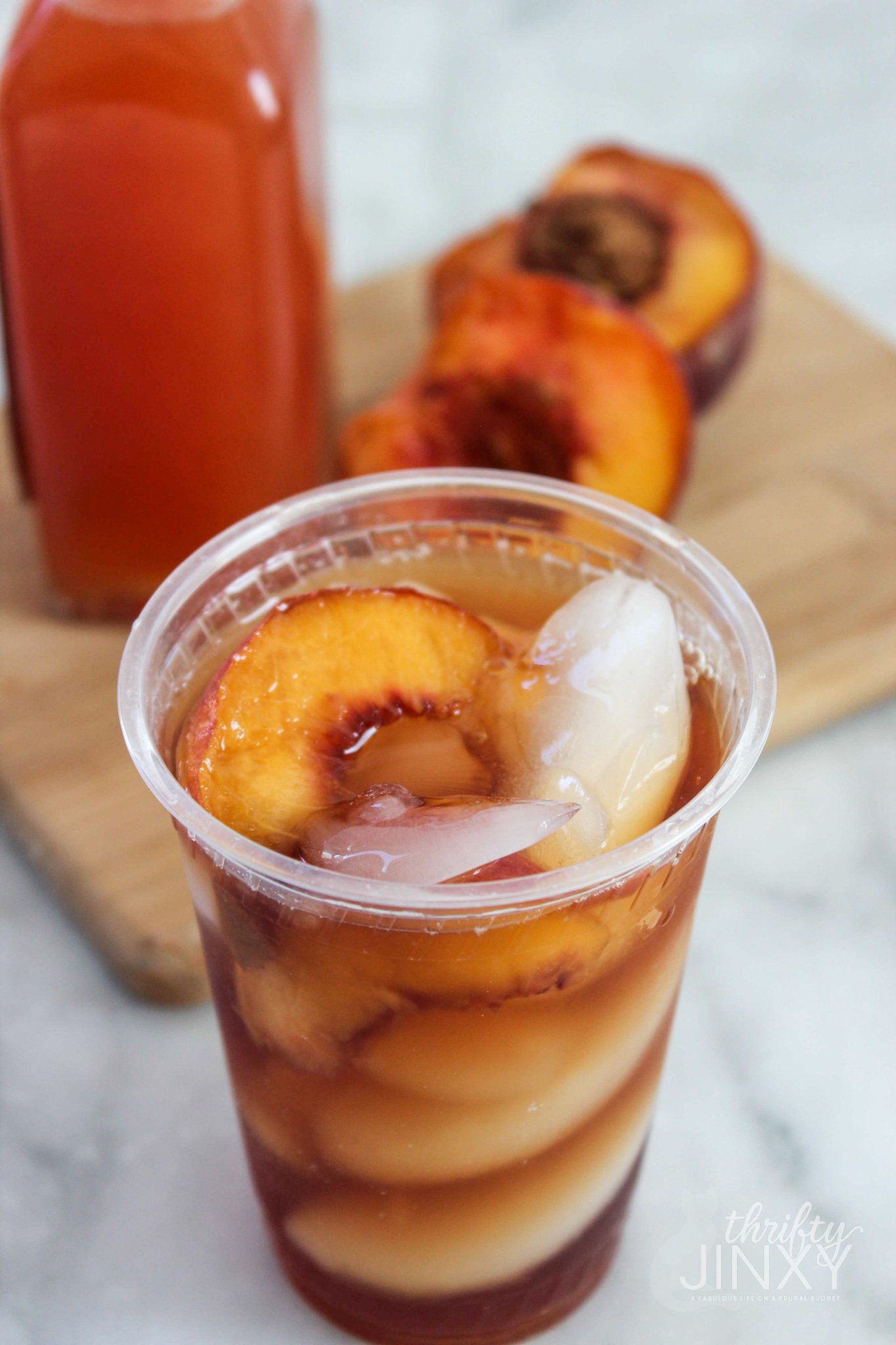 Copycat Sonic Peach Iced Tea in plastic cup with fresh peaches on cutting board in background.