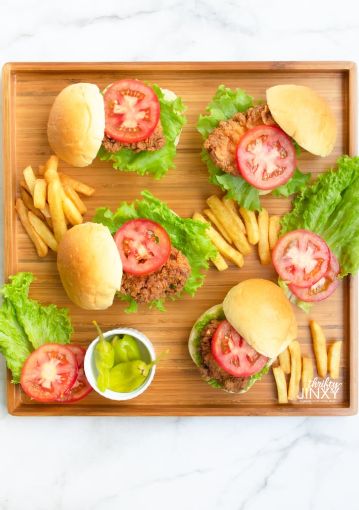 Crispy Fried Chicken Sandwiches with lettuce and tomato on bamboo tray with french fries and banana peppers on the side