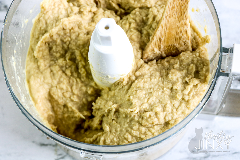 mixing hummus with wooden spoon in the bowl of a food processor.