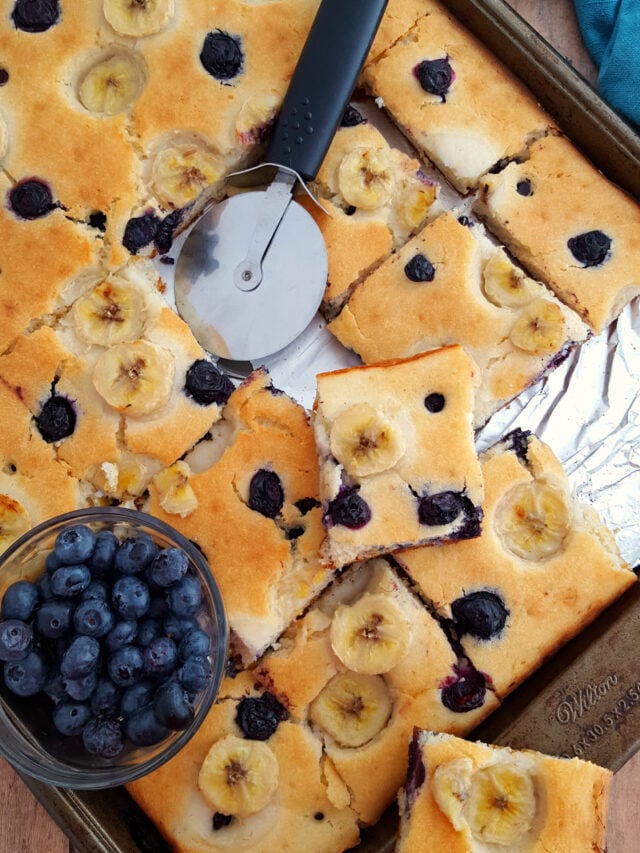 Sheet Pan Blueberry Pancakes with Bananas with a bowl of blueberries and a pizza cutter.