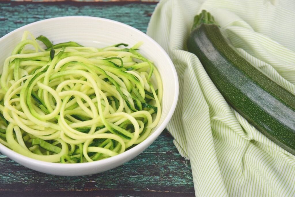 zoodles in bowl next to fresh zucchini