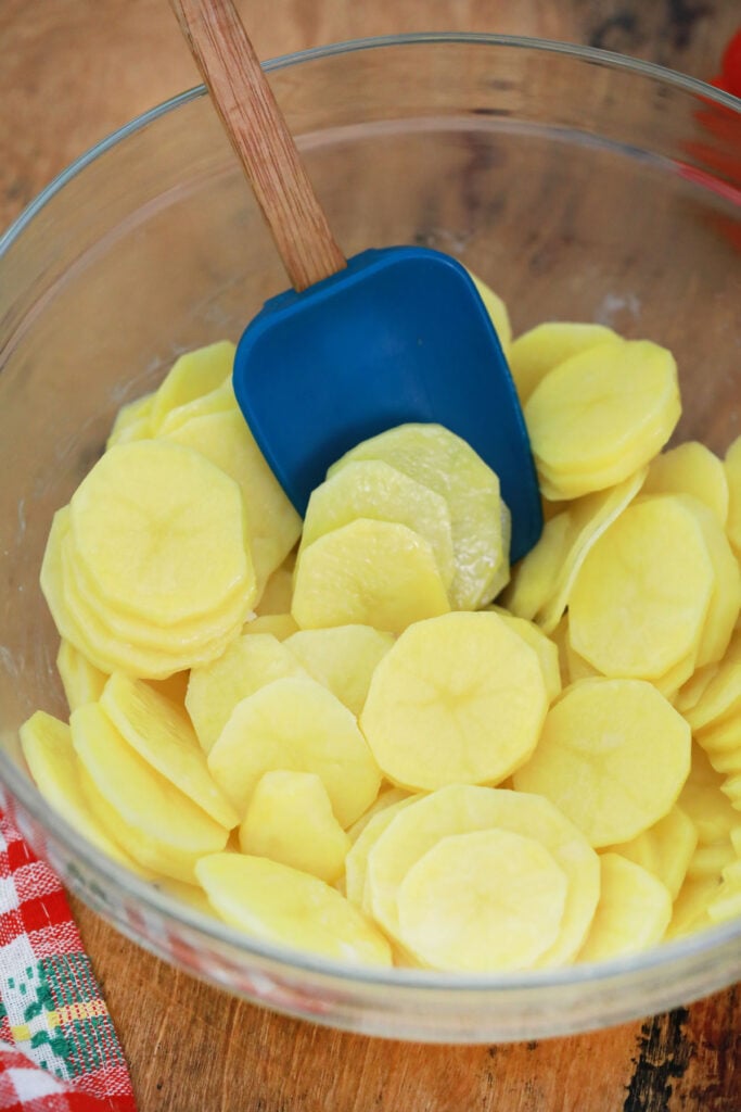 Sliced potatoes in bowl with blue spatula