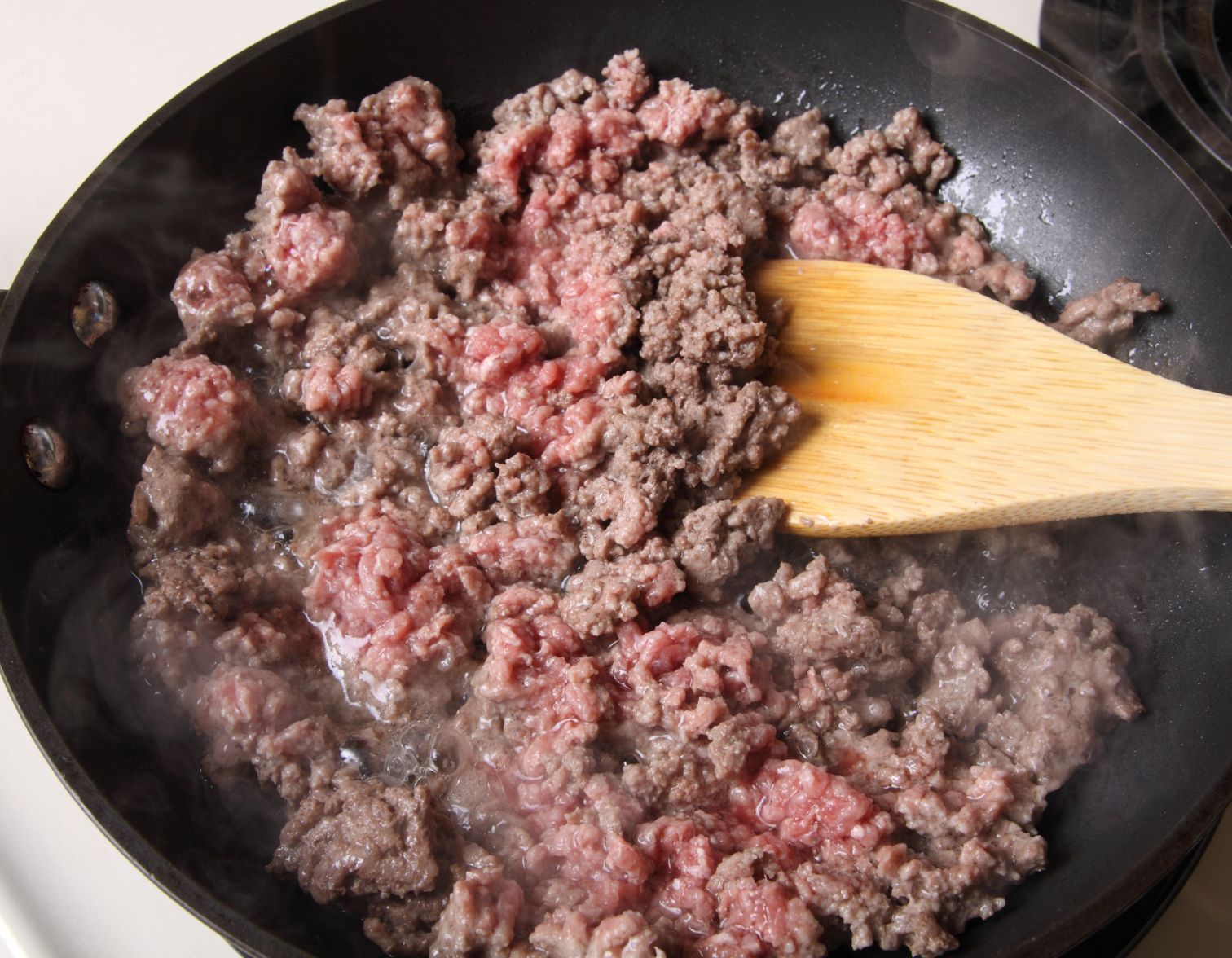 browning ground beef in skillet with wooden spoon