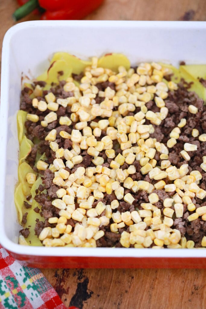 sliced potatoes, ground beef and corn layered in casserole dish