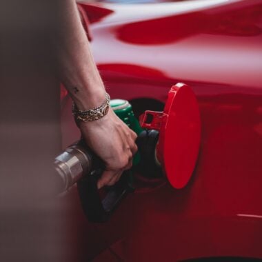 hand on pump filling up red car with gas
