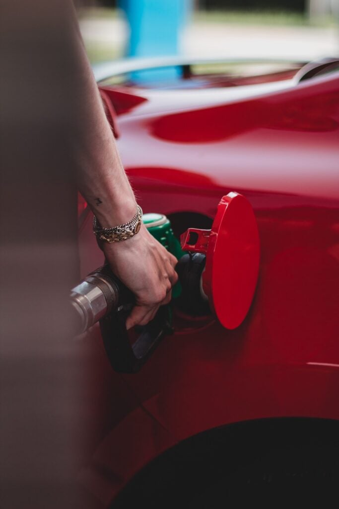 hand on pump filling up red car with gas