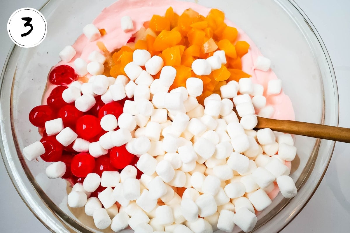 adding marshmallows and cherries to fruit salad.