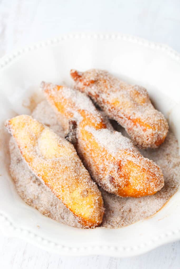rolling biscuit dough churros in white sugar and cinnamon