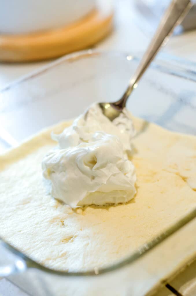 adding cream cheese to a layer or crescent rolls in glass casserole dish