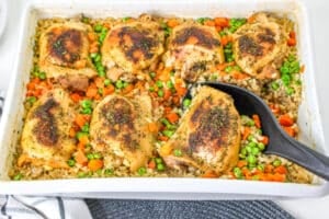 Chicken and Brown Rice Casserole in white baking dish with serving spoon.