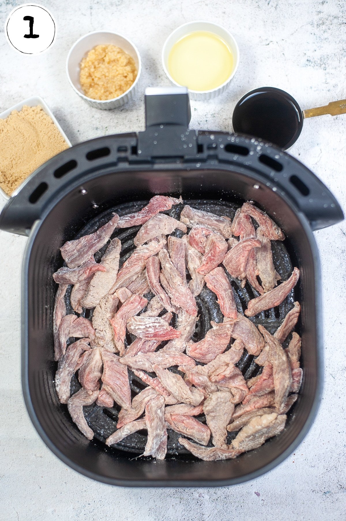 Flank steak coated with corn starch in air fryer basket.
