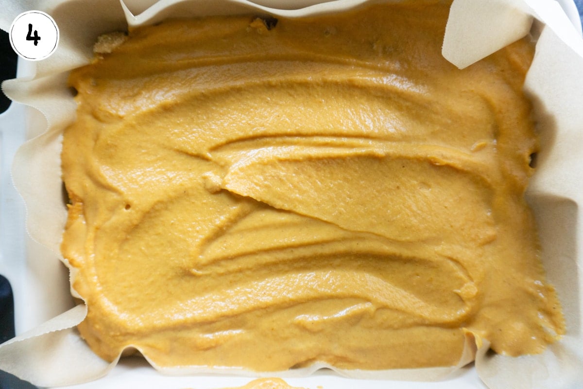 pumpkin bar batter spread in bottom of pan lined with parchment paper.