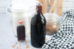 Homemade Maple Syrup in glass bottle next to containers of maple extract and brown sugar.