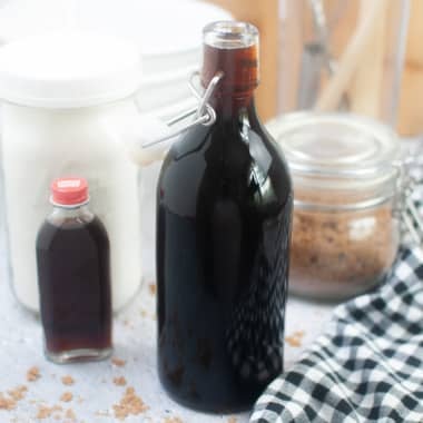 Homemade Maple Syrup in glass bottle next to containers of maple extract and brown sugar.
