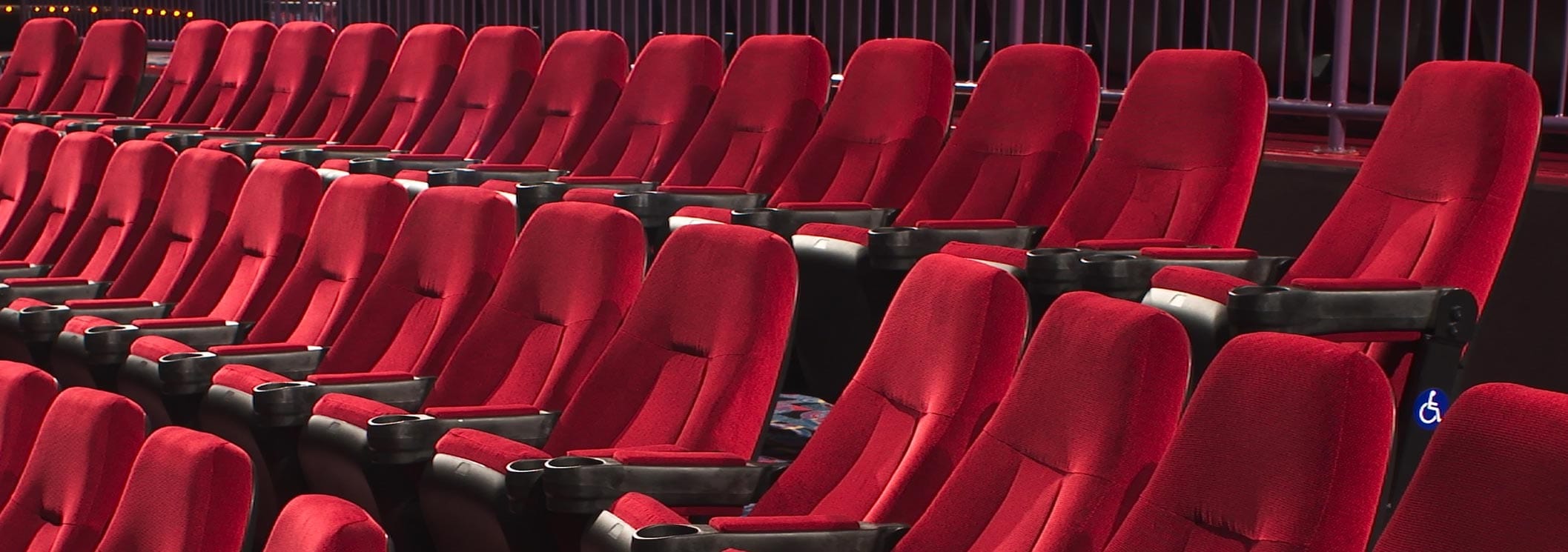 Rows of empty red theater seats with armrests and cup holders, set in a dimly lit auditorium.