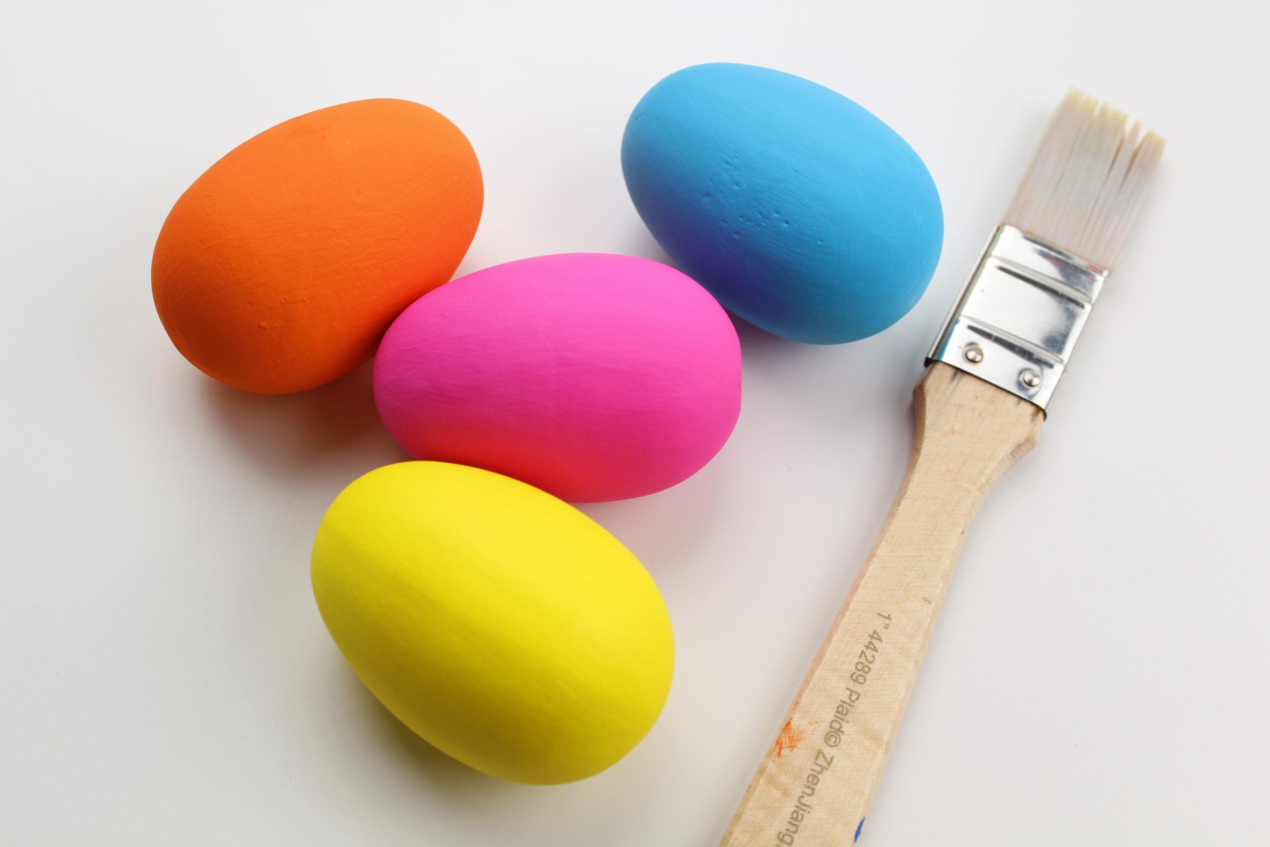 Wooden eggs painted in bright colors next to painbrush.