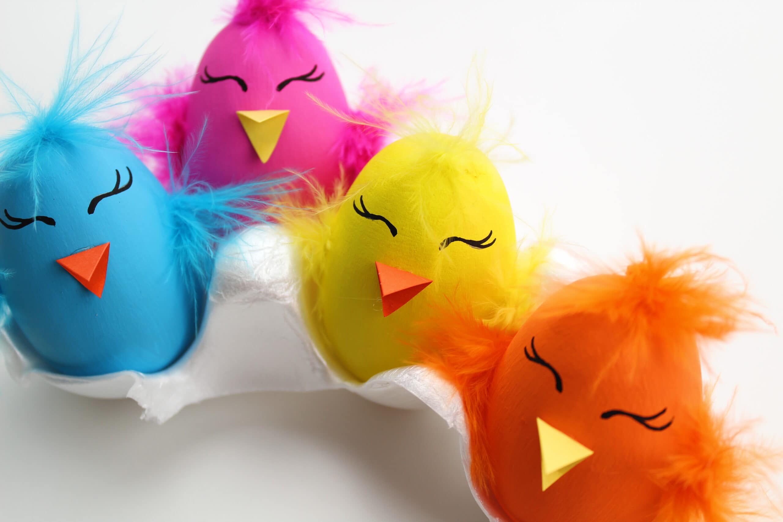 Brightly painted wooden Easter Eggs made to look like chicks with feathers and construction paper beak.