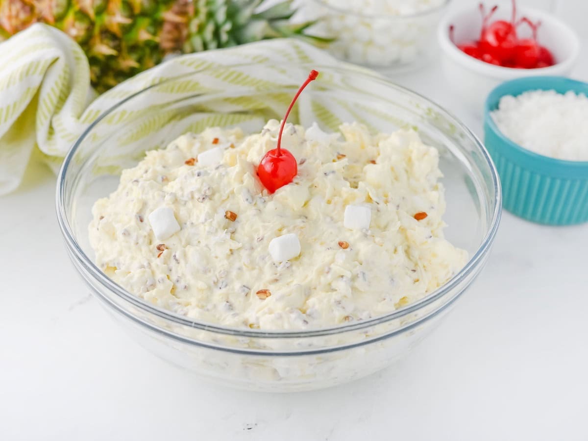 Piña Colada Marshmallow Salad in glass bowl topped with a maraschino cherry.
