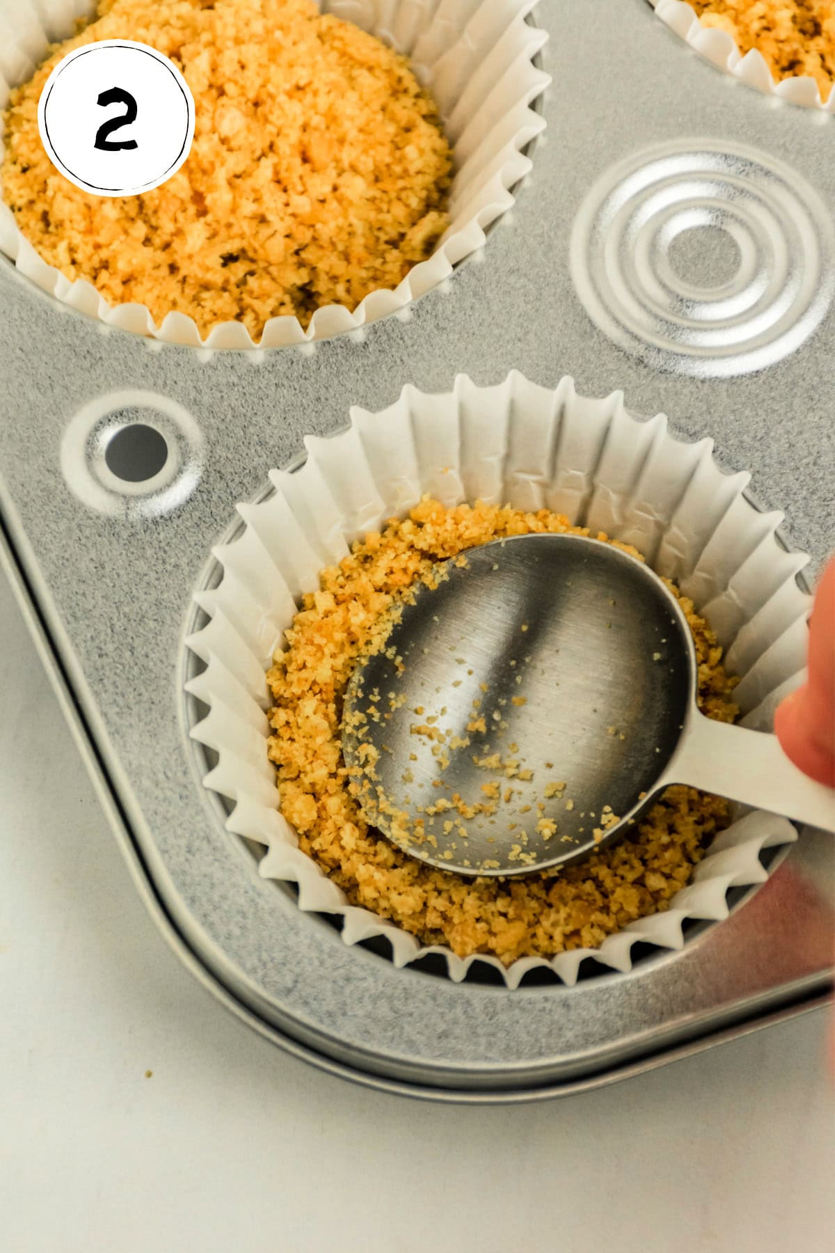 Pressing graham cracker crust into paper liners in cupcake tin.