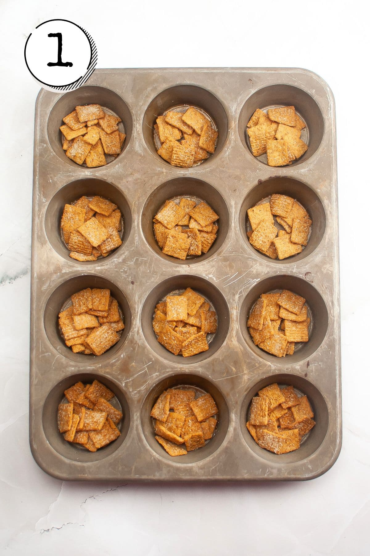 Lightly spraying a muffin tin with oil, dividing cereal into 12 equal portions and placing 1 portion in each cavity.