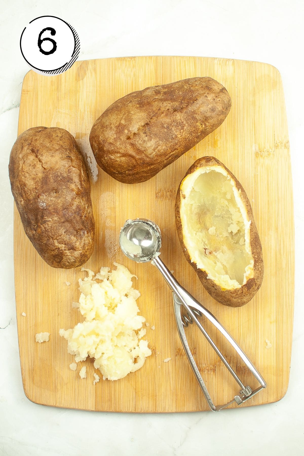 Removing the insides of the potatoes using a baking scoop.